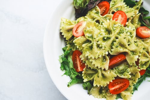 Pasta with pesto and veggies on a white plate