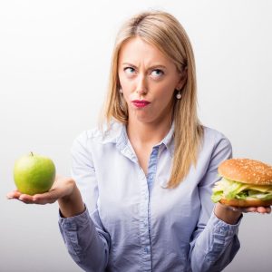 woman holding hamburger in one hand and apple in another