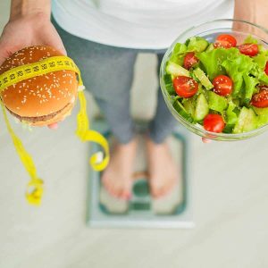 Person on the scale with salad and burger with measuring tape