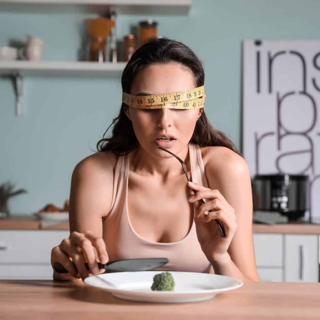 woman with measuring tape over eyes in pink shirt eating 1 Brussels sprout