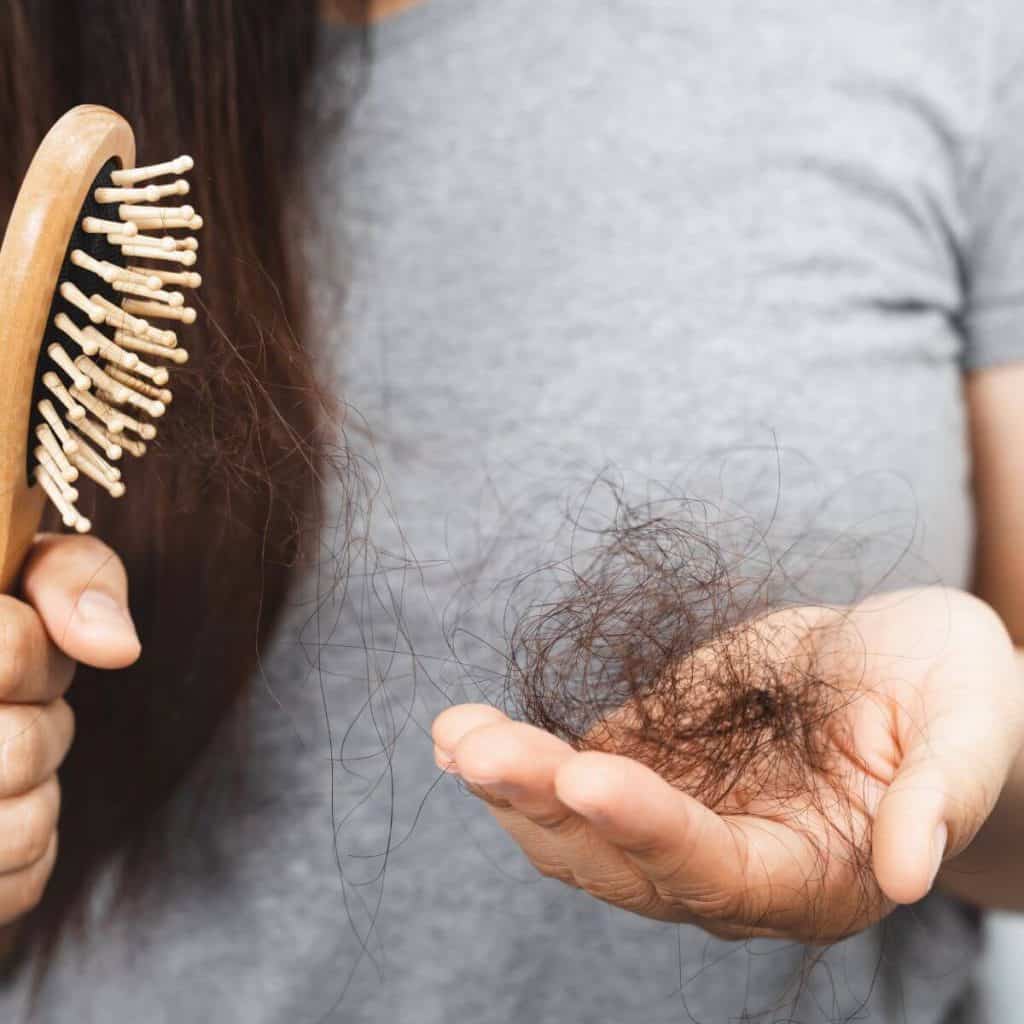 woman with brown hair holding hair brush and clump of hair