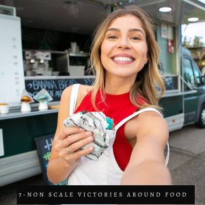 woman holding a burger in red shirt and white overalls