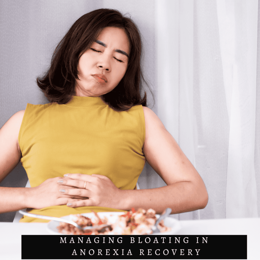 woman holding her stomach in yellow shirt with the words managing bloating in anorexia recovery